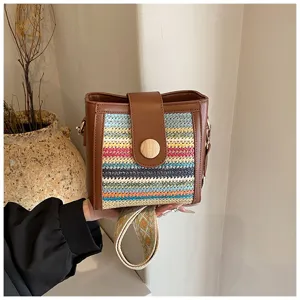 Close-up detail view of woven bucket bag featuring colorful pattern, brown leather trim, and wide strap.