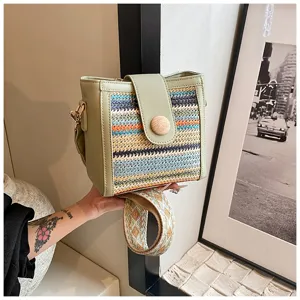 Close up view of the woven bucket bag featuring green leather trim and wide shoulder strap.