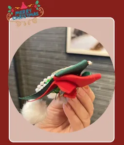 Close-up detail of Christmas hair clip with red green ribbon pearls and white pompom.