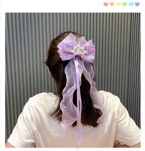 Purple sequin bow hair clip detail showing sparkling crown design and long flowing ribbons clearly.