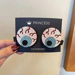 Nahaufnahme von gruseligen Augapfel-Haarspangen mit Glitzerdetails auf Karte, Party-Accessoire.
