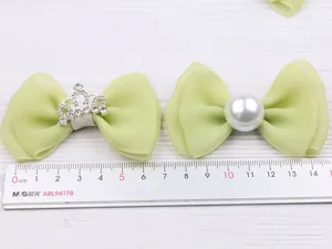 Gros plan de pinces à cheveux nœud en tulle vert avec couronne strass et perle.