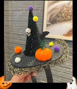 Halloween witch hat headband detail view, showcasing mini pumpkin, skull and colorful pom-poms.