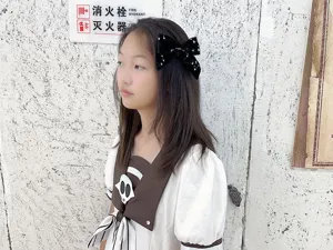 Dettaglio di una forcina con fiocco in velluto nero e stelle bianche, indossata da una bambina.