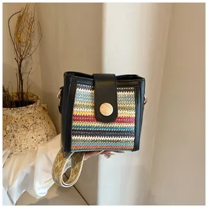 Woven bucket bag detail showcasing colorful straw texture, black leather trim and wide strap.