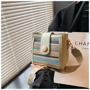 Detailed view of fashionable woven bucket shoulder bag with wide strap and wooden button.