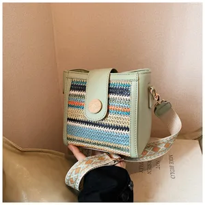 Detailed view of the woven bucket shoulder bag with green leather trim and wide strap.