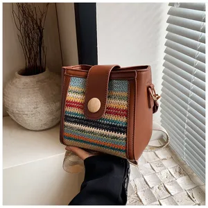 Close up of a woven bucket bag with brown PU leather trim, wooden button and wide strap.
