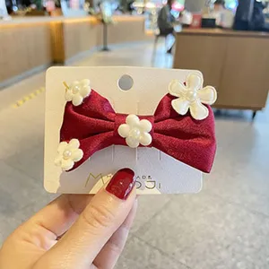 Nahaufnahme einer niedlichen roten Stoff Schleife Haarspange mit weißen Blumen und Perlen.