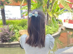 Detailansicht einer süßen hellblauen Stoff-Schleifen-Haarspange mit weißen Blumen, im Freien.