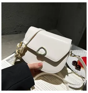 Nahaufnahme der weißen Ledersatteltasche mit eleganter Metallschnalle und Seidenschal.