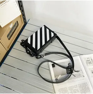 Vue détaillée d'un sac bandoulière boîte rayé noir et blanc avec chaîne grosse sur table.