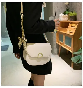 Detailaufnahme der weißen Ledersatteltasche mit goldenen Beschlägen und Dekoschalriemen.