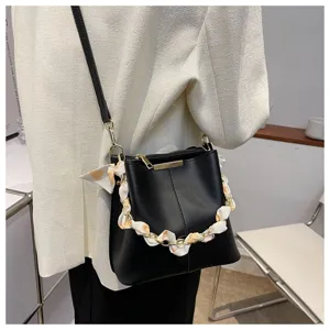 Nahaufnahme einer schwarzen Eimer-Handtasche mit stilvollem Kettenhenkel und Dekoschal.