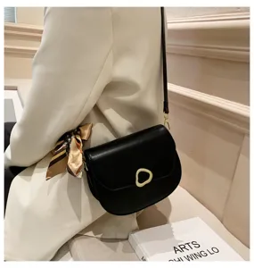 Detailansicht einer eleganten schwarzen Damensatteltasche mit Goldschnalle und Schal.