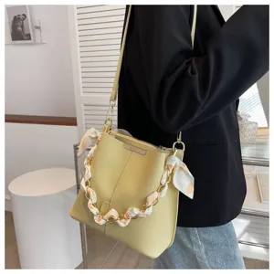 Detailaufnahme der gelben Beuteltasche mit Kettengurt und Seidenschal fuer den modischen Alltag.