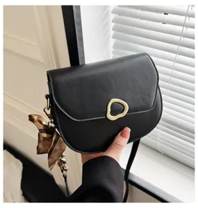 Nahaufnahme einer stilvollen schwarzen Satteltasche mit goldener Schnalle und Schal.