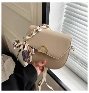 Nahaufnahme einer stilvollen beigen Satteltasche mit schicker Seidentuch-Kette und Metallschließe.