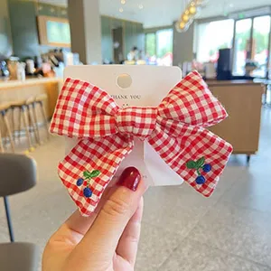 Detailed view of a red and white checkered bow hair clip with cute blue berry embroidery.