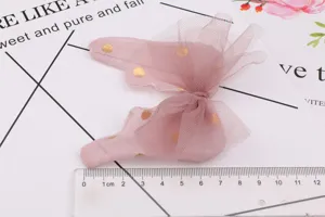 Détail de pince à cheveux lapin en tulle rose, avec des pois dorés et un tissu léger.