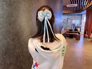 Detailed view of a light blue mesh bow hair clip with long ribbons and a pearl heart.