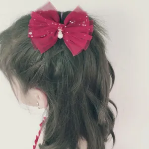 Primo piano dell'elegante fiocco per capelli rosso in tulle con paillettes e perla pendente.