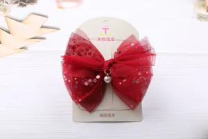 Dettaglio accessorio per capelli fiocco in rete e paillettes rosse con ciondolo perlato.