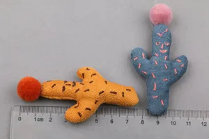 Nahaufnahme niedlicher Stoff-Kaktus-Accessoires mit Pompons für DIY-Haarspangen oder Basteln.
