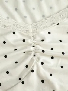 Close-up fabric detail of white polka dot top featuring V-neck lace trim and gathered texture.