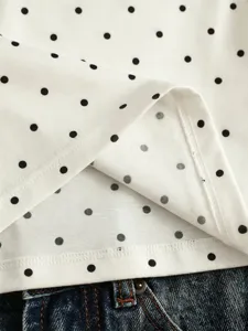 Close-up detail of white fabric with black polka dots, showing fine stitching and smooth texture.