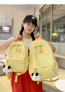 Nahaufnahme des gelben Stoffrucksacks mit bunter Stickerei und niedlichem Panda-Anhänger.