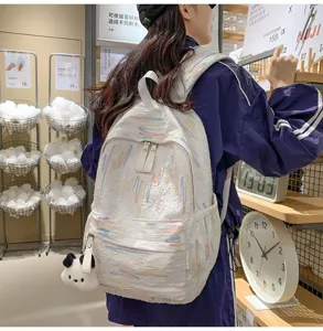 Details des weißen Stoffrucksacks mit bunter Pinselstrich-Bestickung und süßem Plüsch-Anhänger.