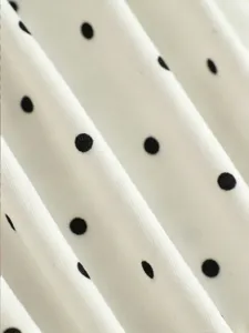 Close-up detail of white fabric with black polka dots, soft texture and draping folds.
