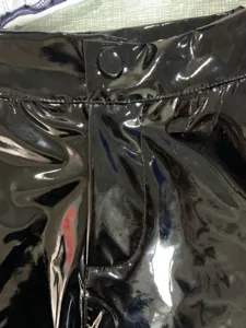 Close-up detail of black patent leather shorts, glossy PU fabric surface, fly button and zipper.