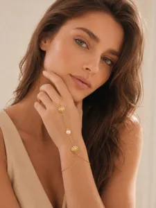 Elegante pulsera de mano dorada con dijes de concha, circones brillantes y una perla.