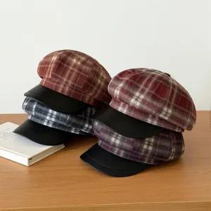 Detailed view of stylish plaid newsboy hats with leather brims, neatly stacked on wooden surface.