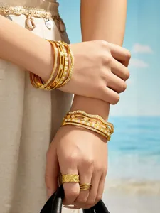 Detail shot of multi-layer wavy gold metal bracelets with cubic zirconia and floral motifs on arm.
