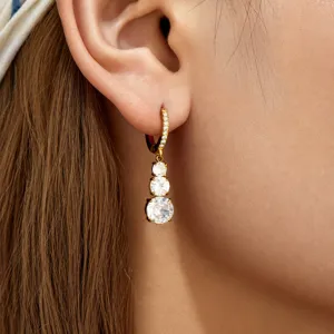 Close-up detail of golden triple zircon drop earrings worn on ear, elegant and shiny design.
