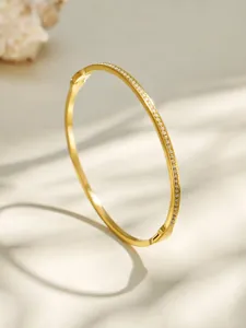Close-up of a sleek gold-tone metal pave rhinestone oval bangle bracelet detail shot.