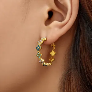 Detalle de pendientes de aro dorados chapados con motivo de trébol y circonitas.