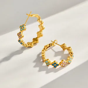 Detalle de pendientes de aro de acero dorado con circonitas de colores en forma de trébol.