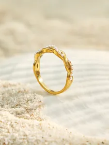 Detailansicht des unregelmäßig gewundenen vergoldeten Rings mit kleinen weißen Perlen.