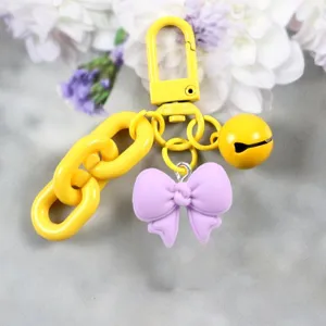 Süßer gelber Schlüsselanhänger mit lilanem Schleifen-Anhänger, Karabiner und Glocke.