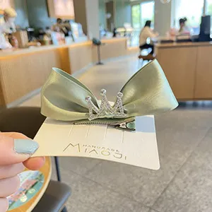 Detailed shot of a light green satin bow hair clip with a sparkly rhinestone crown for kids.