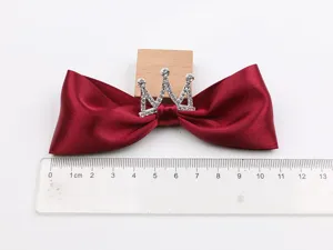 Close up of a wine red satin bow hair clip with a sparkling rhinestone crown detail.