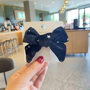 Detailed view of a cute black velvet bow hair clip featuring lovely white star patterns for girls.