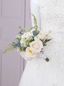 Gros plan détaillé du bouquet de mariée en roses blanches artificielles et baies bleues.