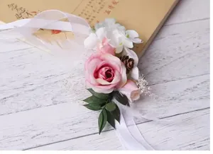 Romantic pink rose wrist flower wedding corsage with pine cones, feathers and ribbon.