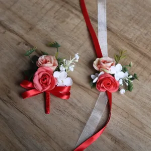 Close-up details of artificial rose wedding boutonniere and wrist flower set with red ribbons.
