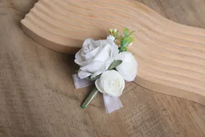 Gros plan détaillé d'une élégante boutonnière de rose artificielle blanche avec des feuilles vertes.